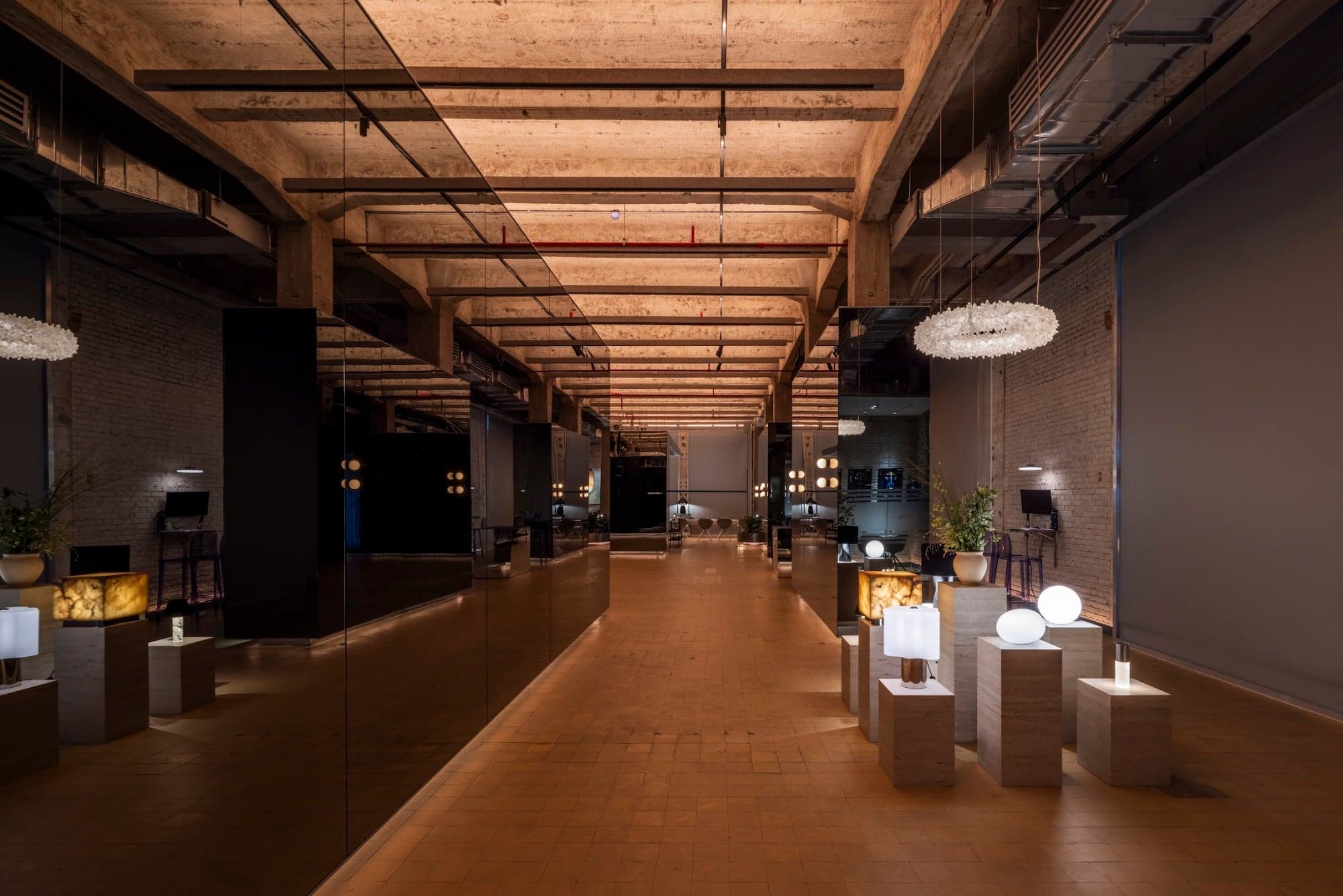 Inside the Unios HCMC Experience Centre: a long hall with exposed concrete beams, mirrored black panels and lamps on stone plinths, warmly lit
