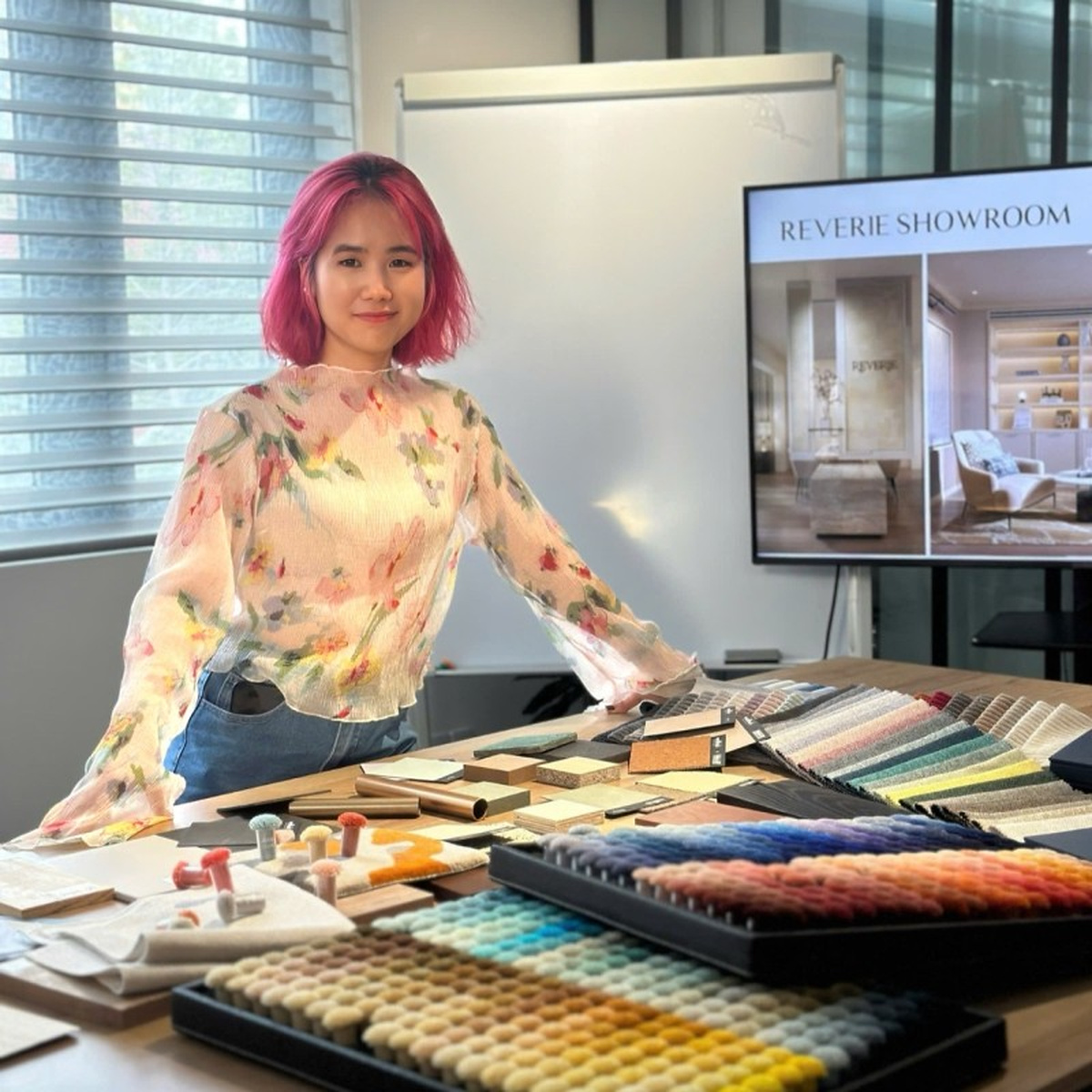 Yen Do at a table of fabric and material swatches, with the Reverie Showroom slide on the screen behind her