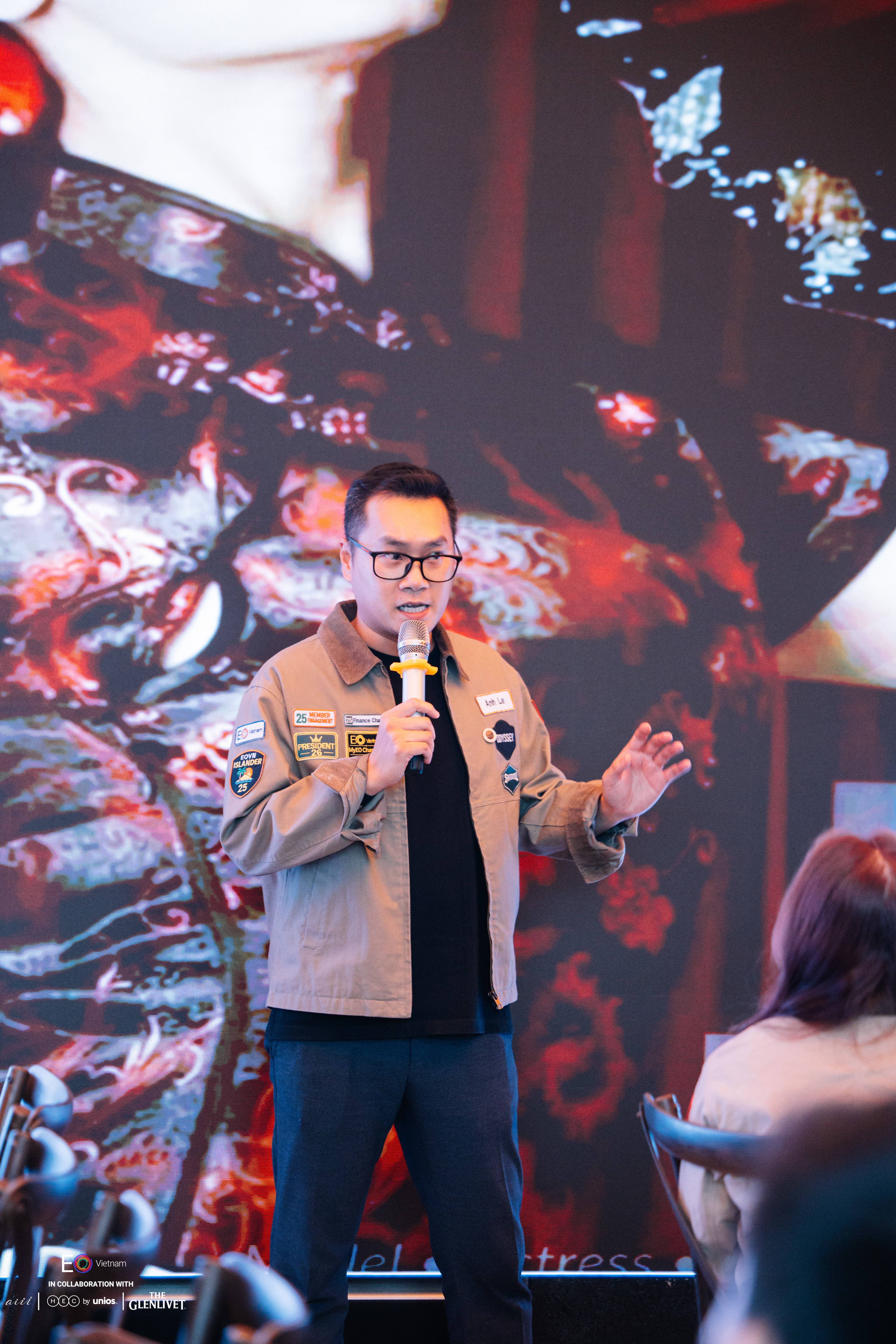 Le Tuan Anh speaking on stage at an EO Vietnam event, microphone in hand